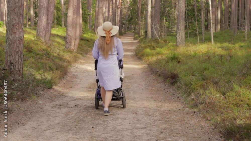 Young Female with Stroller Walks on Forest Road in Casual Purple Dress Young Female with Stroller Walks on Forest Road in Casual Purple Dress