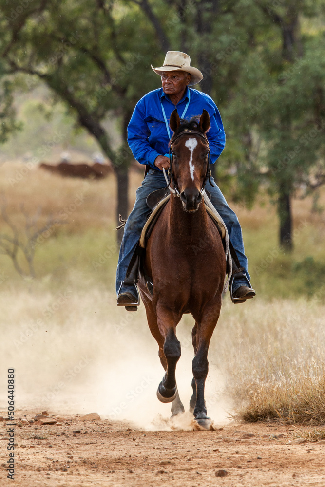 An aboriginal stockman cantering on horse kicking up dust An aboriginal stockman cantering on horse kicking up dust