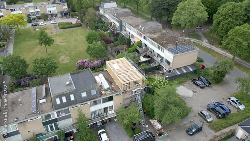 Aerial overview of wooden frame of roof structure under construction in a busy suburban neighborhood - Drone flying backwards photo