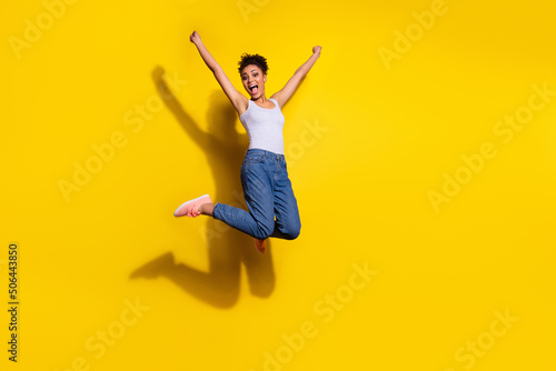 Full body portrait of overjoyed pretty girl jump raise fists celebrate luck success isolated on yellow color background