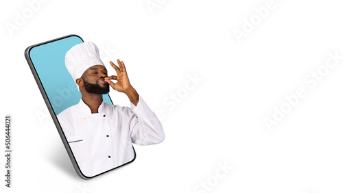 Black Male Chef Kissing Fingers While Peeking Out Of Big Smartphone Screen photo
