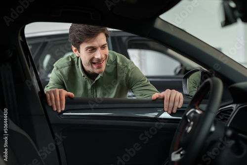 Handsome young man looking through window inside new car, checking it before purchase at modern dealership store © Prostock-studio