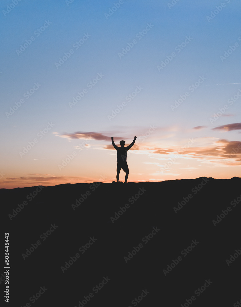 Silueta de deportista, en la montaña con los brazos levantados, con expresión de victoria y felicidad. Fotografía vertical con espacio para texto.