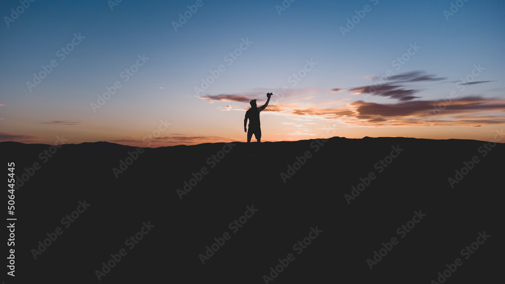 Silueta de un hombre con la cámara, en lo alto de la montaña, con un bonito atardecer. Fotografía horizontal con espacio para texto.