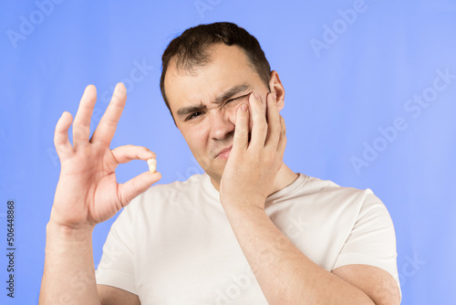 Man in a white T-shirt on a blue background holds a wisdom tooth in his hands after surgical tooth extraction.Man after an operation to remove wisdom teeth.Pain in wisdom teeth, concept of dentistry