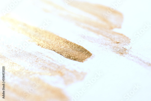Gold makeup streaks with metallic glitter on white background.