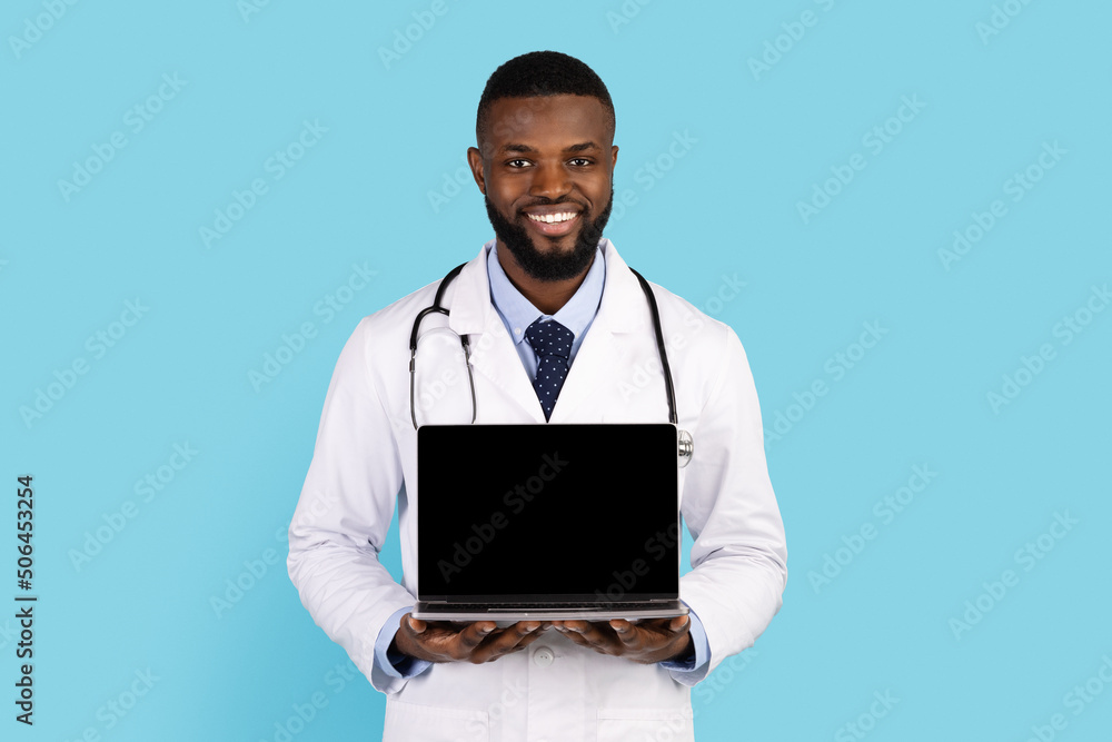 Smiling Black Doctor In White Coat Holding Laptop With Blank Screen Smiling Black Doctor In White Coat Holding Laptop With Blank Screen
