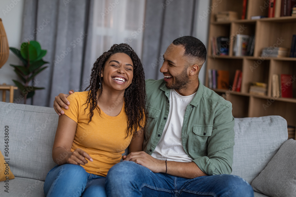 Happy young african american family embracing and laughing while resting on couch in living room, copy space