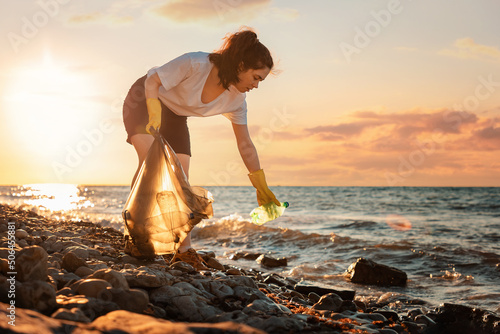 A female volunteer is collecting plastic garbage on the seashore. Cleaning of the coastal zone. Copy space. The concept of Earth Day and environmental conservation photo