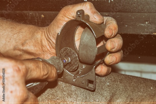 The hands of a man holding a Dremel instrument.Metalworking. Workshop. Production of products. Carpentry cutting tool.Car tuning and repair.Using a Dremel to cut out a metal part.Male hands. photo