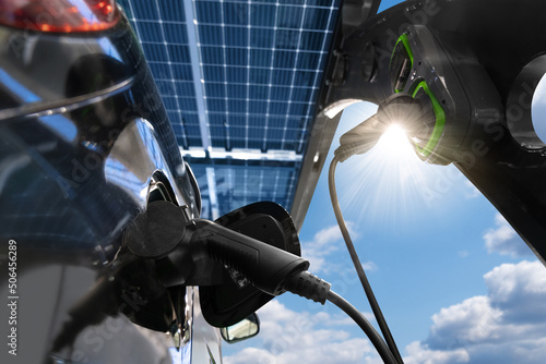 Electric car is charging from a charging station that takes energy from solar panels. Close up