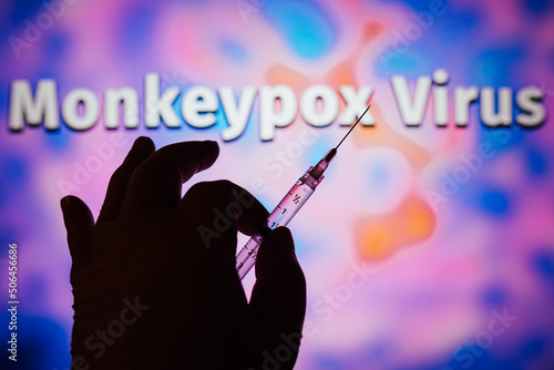 A hand holding a medical syringe with the word Monkeypox in the background. Is a viral disease that occurs mainly in central and western Africa. It's called monkeypox. photo