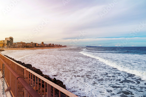 view of the coastal city and sea waves with a breakwater and a mountain in the clouds in the background