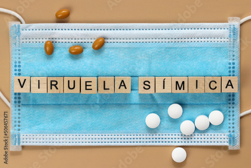 Viruela símica is the name of the monkeypox virus in Spanish. The word is laid out with wooden cubes on a surgical face mask. There are various pills lying around. photo