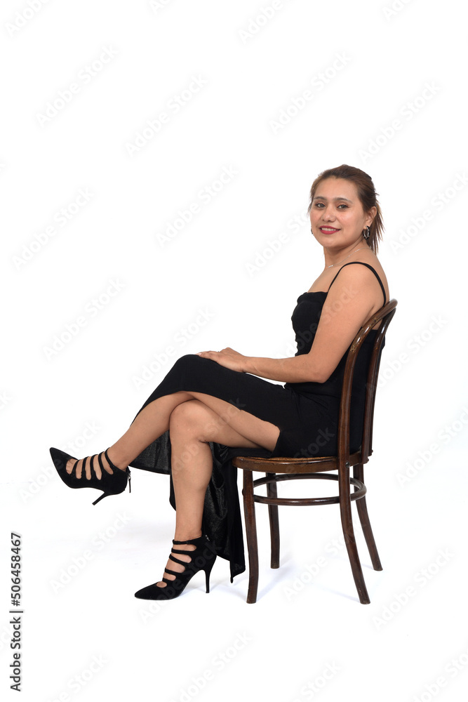 side view of a woman sitting on chair with dress and heeled shoes looking at camera and legs crossed on white background side view of a woman sitting on chair with dress and heeled shoes looking at camera and legs crossed on white background