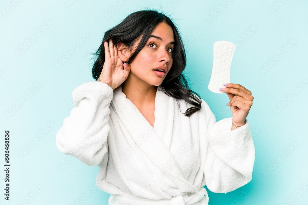 Young caucasian woman holding sanitary napkin isolated on pink background trying to listening a gossip.