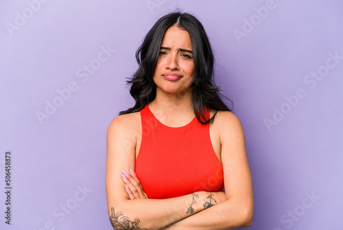 Young hispanic woman isolated on purple background frowning face in displeasure, keeps arms folded.