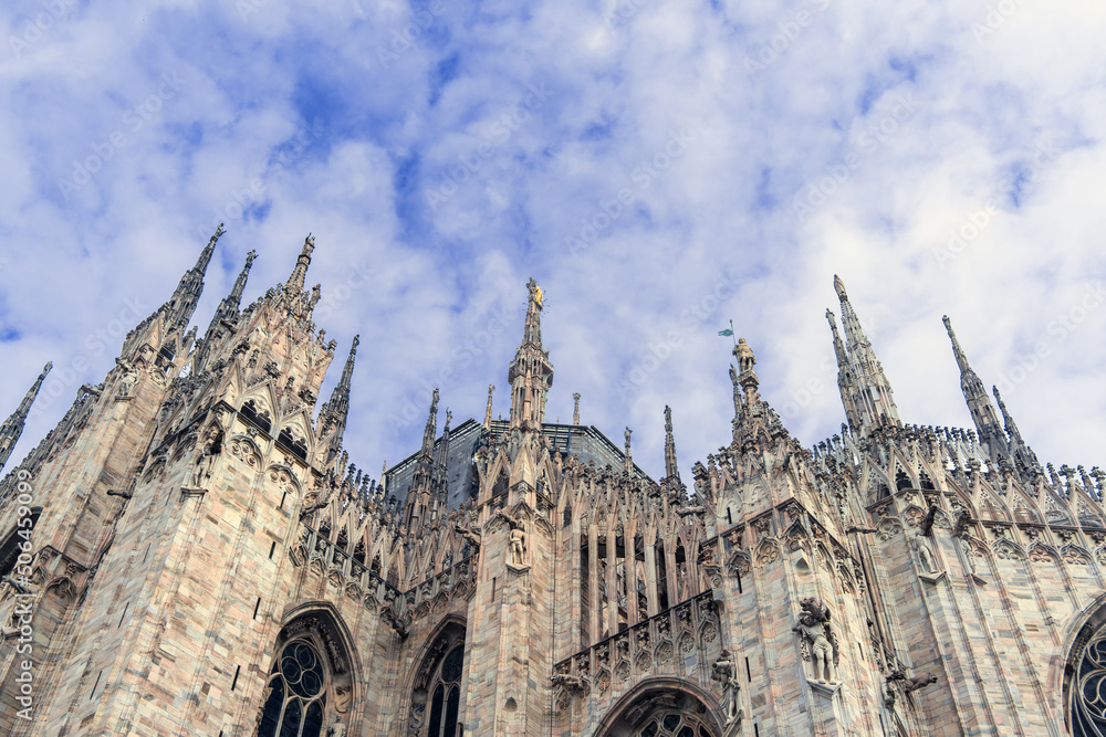 Wall of the famous Cathedral of the Nativity of the Blessed Virgin Mary in Milan, Italy, under a cloudy blue sky in the early morning, Europe tourist attractions