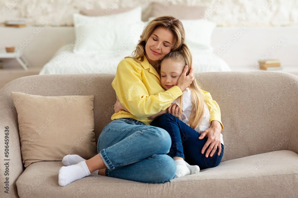 Loving Mom Hugging Little Daughter Sitting On Sofa At Home Loving Mom Hugging Little Daughter Sitting On Sofa At Home