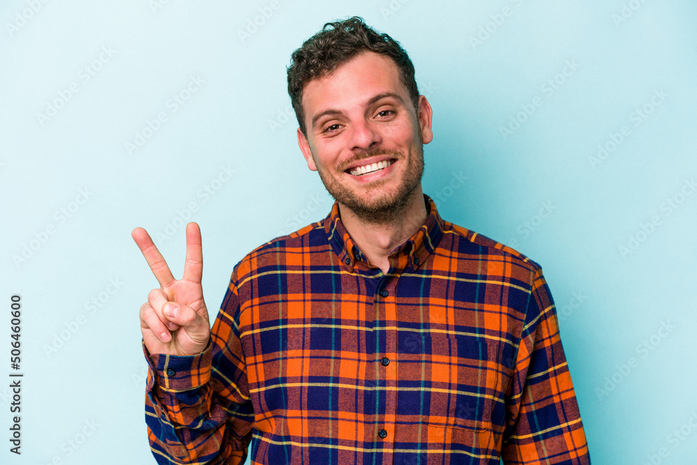 Young caucasian man isolated on blue background showing victory sign and smiling broadly. Young caucasian man isolated on blue background showing victory sign and smiling broadly.