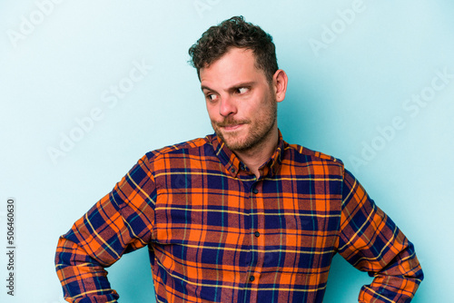Young caucasian man isolated on blue background confused, feels doubtful and unsure.