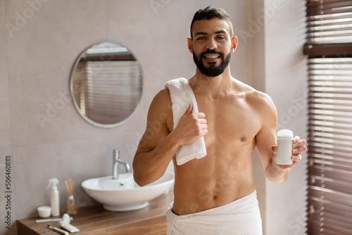 Handsome young guy standing with deodorant bottle in hand