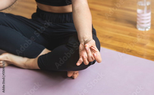 Woman meditating in studio in lotus position with Shuni Mudra yogic hand gesture.