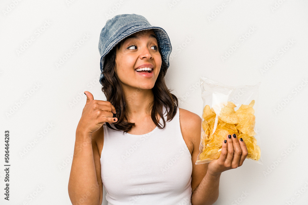 Young hispanic woman holding a bag of chips isolated on white background showing a mobile phone call gesture with fingers. Young hispanic woman holding a bag of chips isolated on white background showing a mobile phone call gesture with fingers.