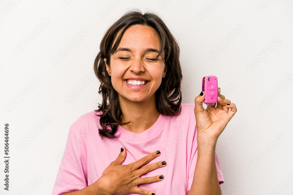 Young hispanic woman holding car keys isolated on white background laughs out loudly keeping hand on chest. Young hispanic woman holding car keys isolated on white background laughs out loudly keeping hand on chest.