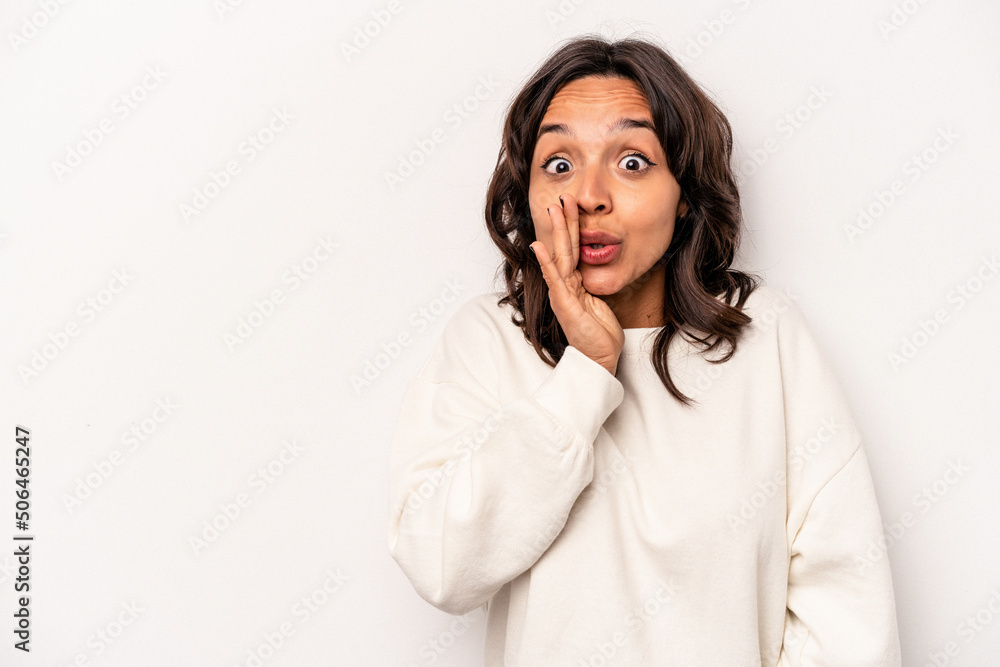Young hispanic woman isolated on white background is saying a secret hot braking news and looking aside