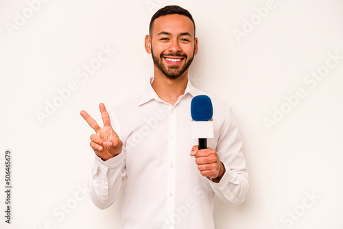 Young hispanic TV presenter isolated on blue background joyful and carefree showing a peace symbol with fingers.