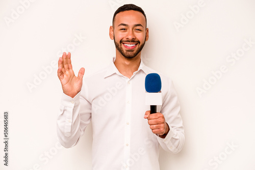 Young hispanic TV presenter isolated on blue background receiving a pleasant surprise, excited and raising hands.