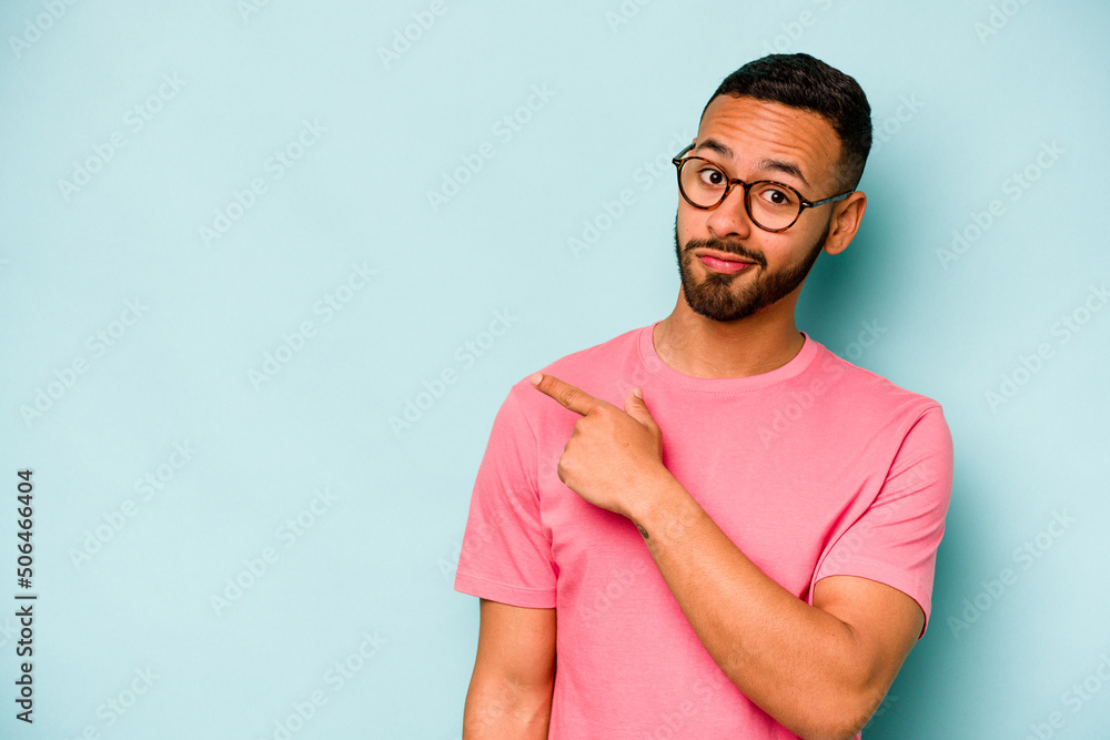 Young hispanic man isolated on blue background smiling and pointing aside, showing something at blank space. Young hispanic man isolated on blue background smiling and pointing aside, showing something at blank space.