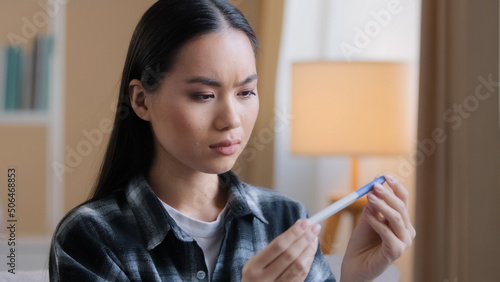Puzzled doubtful Asian woman waiting result of pregnancy test girl worry with unplanned children. Sad unhappy pregnant Korean lady sitting at home problem with about baby unwanted pregnancies reaction