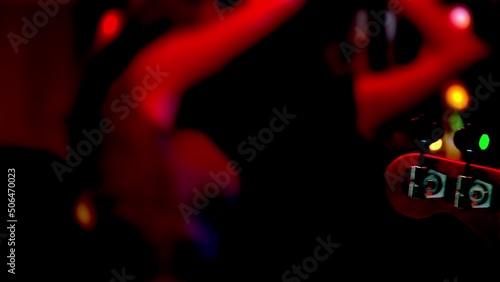 Bass guitar headstock in time of Band live performance with dancing girls on background in a nightclub