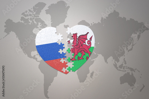 puzzle heart with the national flag of russia and wales on a world map background. Concept.