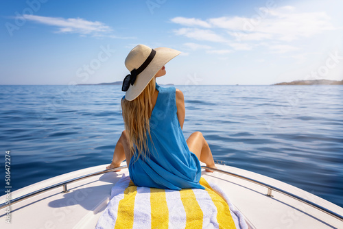 Canvas Print A beautiful, blonde woman with a hat sits on a boat and enjoys the calm sea duri