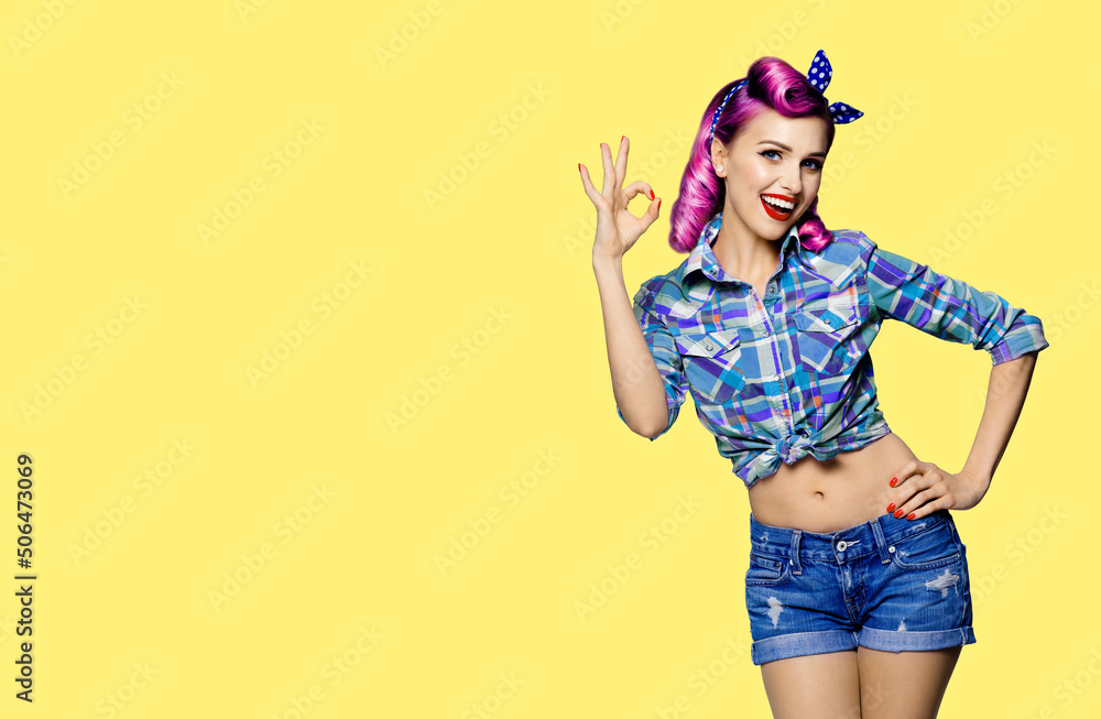 Pin up girl. Portrait photo of excited cheerful smiling red purple hair woman showing ok okay hand sign gesture. Retro and vintage concept. Yellow background. Female model at studio. Pin up girl. Portrait photo of excited cheerful smiling red purple hair woman showing ok okay hand sign gesture. Retro and vintage concept. Yellow background. Female model at studio.