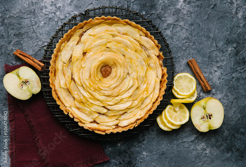 An beautiful apple pie with a lemon swirl and cinnamon stick. The pie is on a black rack and background.