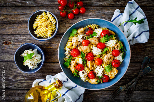 Roasted chicken nuggets, cherry tomatoes, feta cheese and fusilli  served on wooden table

