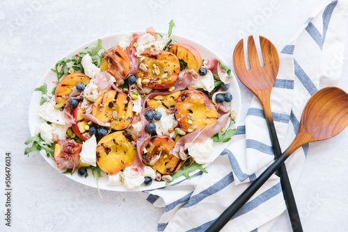 A peach prosciutto salad. On top of the salad is Pistachios, cheese, and blue berries.