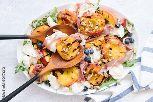 A peach prosciutto salad. On top of the salad is Pistachios, cheese, and blue berries.