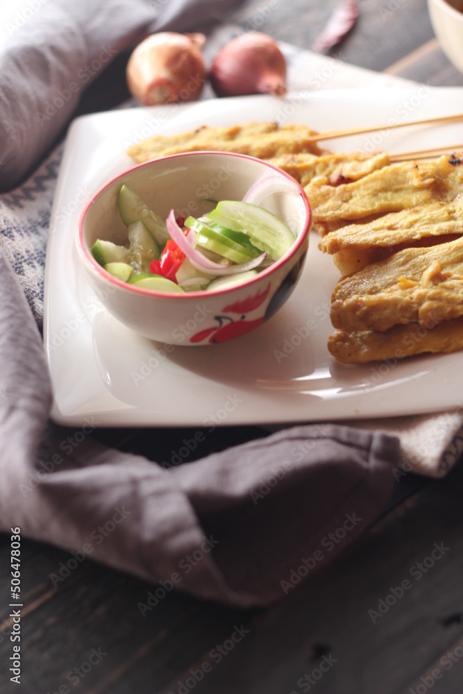 Pork satay served in a white plate with peanut and cucumber dipping sauce. Pork satay served in a white plate with peanut and cucumber dipping sauce.