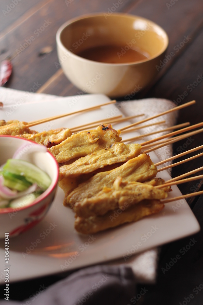 Pork satay served in a white plate with peanut and cucumber dipping sauce. Pork satay served in a white plate with peanut and cucumber dipping sauce.