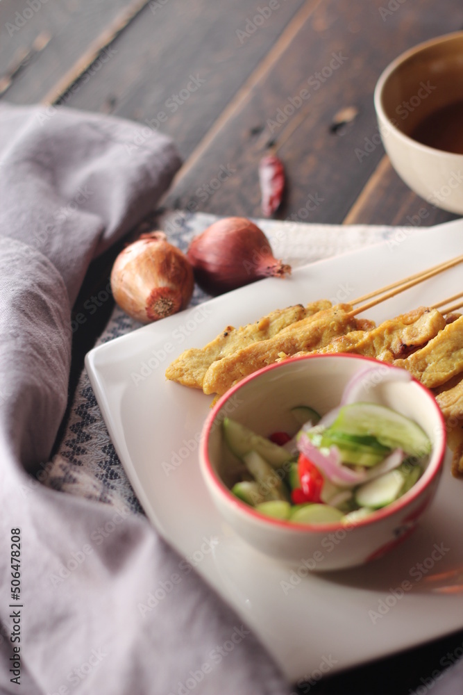 Pork satay served in a white plate with peanut and cucumber dipping sauce. Pork satay served in a white plate with peanut and cucumber dipping sauce.