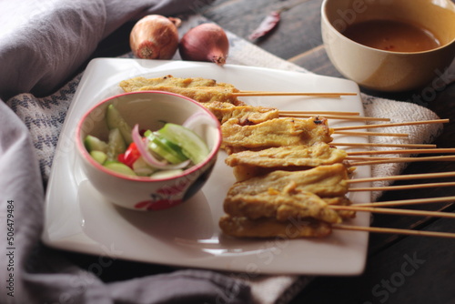 Pork satay served in a white plate with peanut and cucumber dipping sauce.