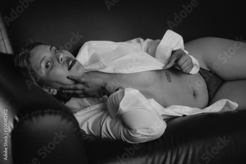 Black and white photo of a woman in a white shirt and lingere on a sofa