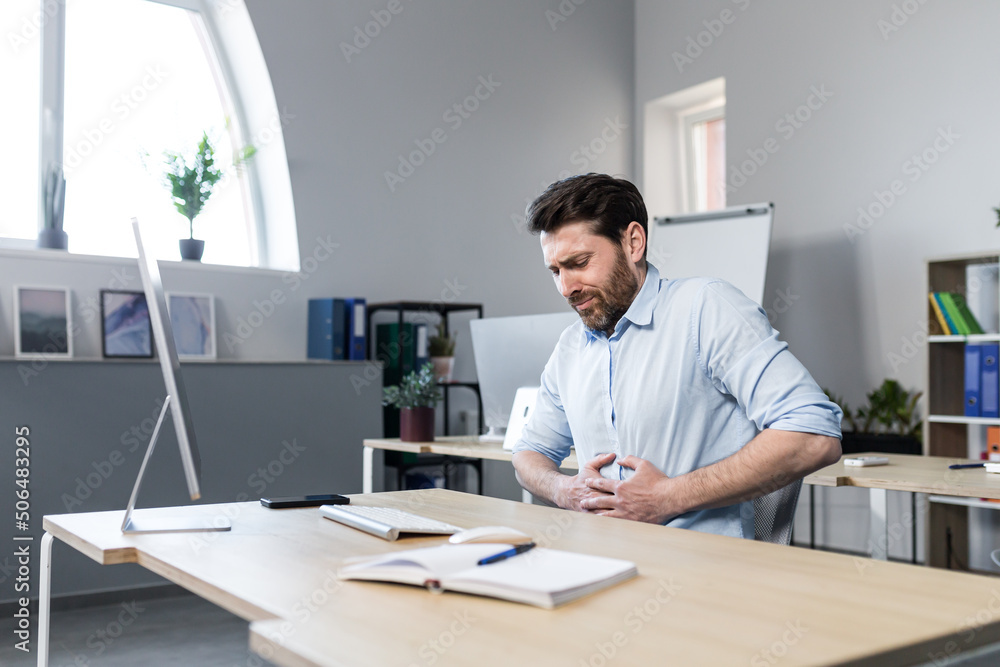 Sick man at work sitting at the table, has severe abdominal pain, businessman unhappy and upset Sick man at work sitting at the table, has severe abdominal pain, businessman unhappy and upset