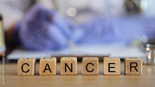 Doctor filling out medical paperwork on background of wooden cubes with word cancer closeup