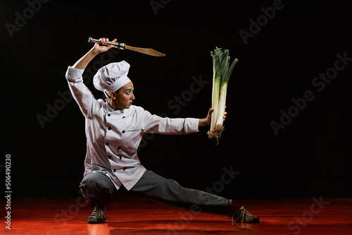 Young female mime artist with knife and leeks performing martial arts pose